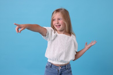 Photo of Cute little girl pointing at something and laughing on light blue background