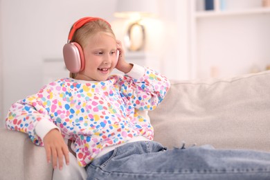 Photo of Smiling little girl in headphones listening to music on sofa at home