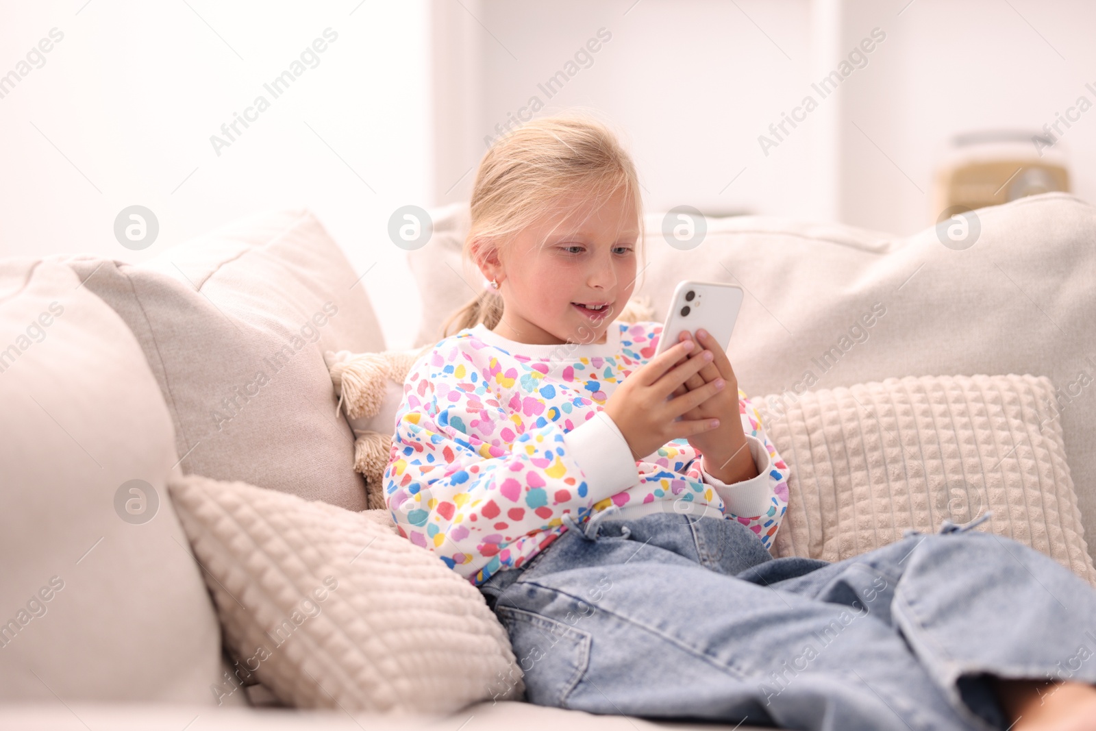 Photo of Smiling little girl with smartphone on sofa at home