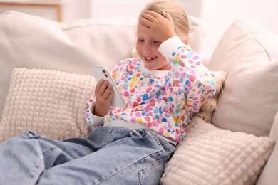 Photo of Smiling little girl with smartphone on sofa at home