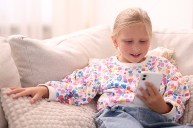 Photo of Smiling little girl with smartphone on sofa at home