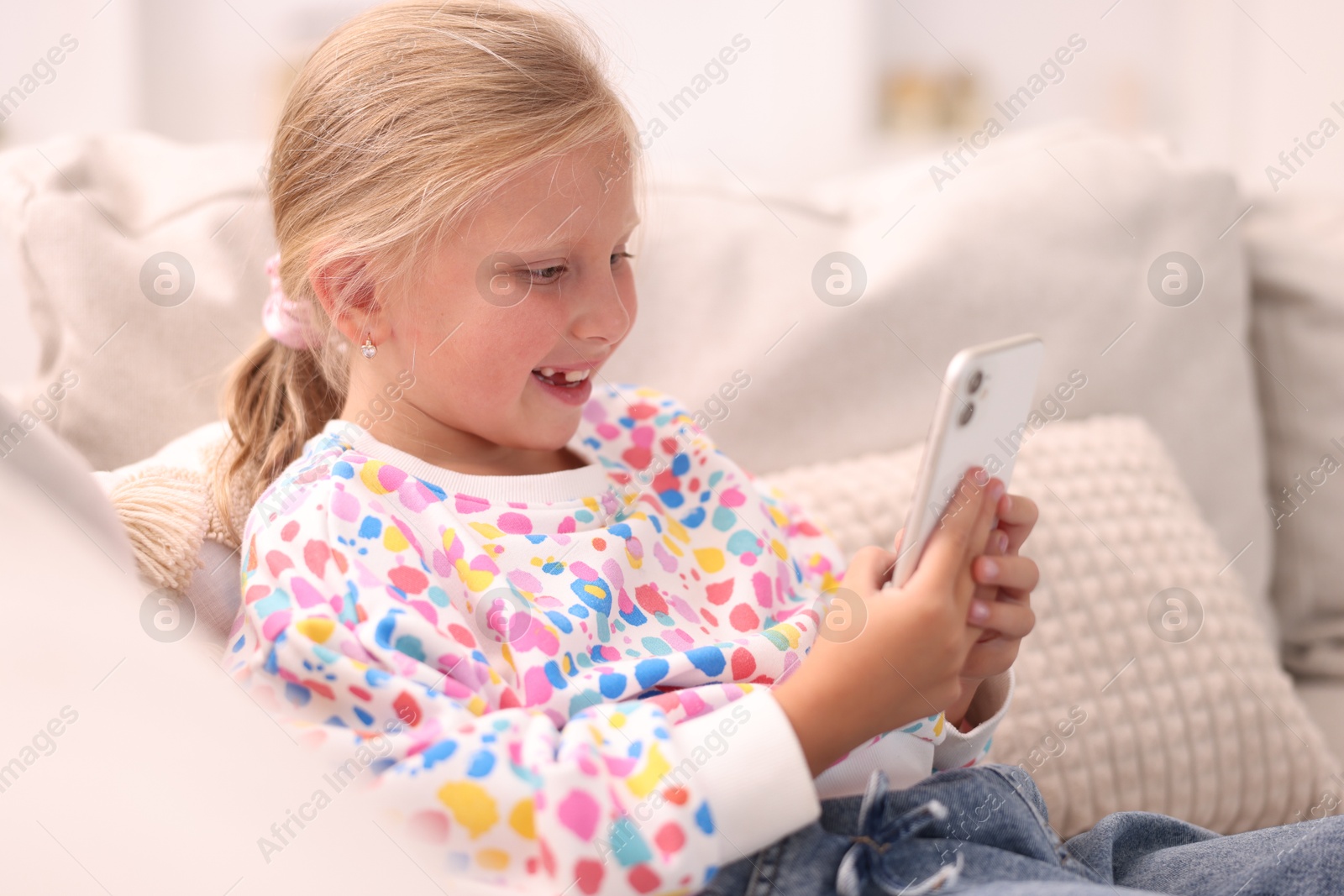 Photo of Smiling little girl with smartphone on sofa at home