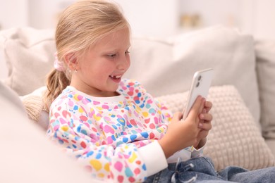 Photo of Smiling little girl with smartphone on sofa at home