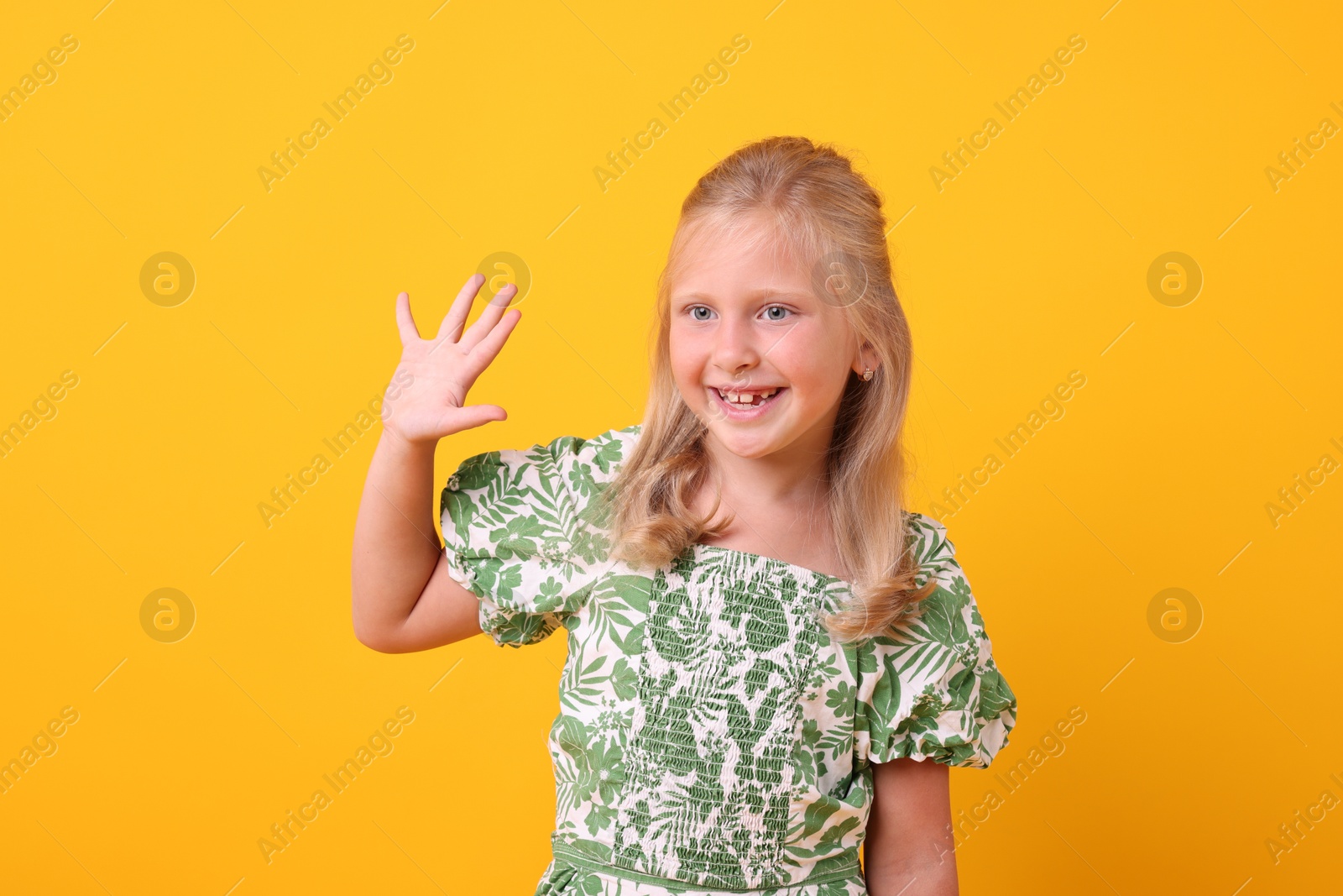 Photo of Smiling little girl waving hello on yellow background