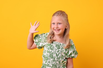 Photo of Smiling little girl waving hello on yellow background