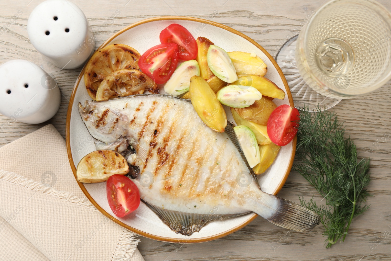 Photo of Tasty roasted flounder fish served with potatoes, tomatoes and lemon slices on light wooden table, flat lay. Homemade seafood dish