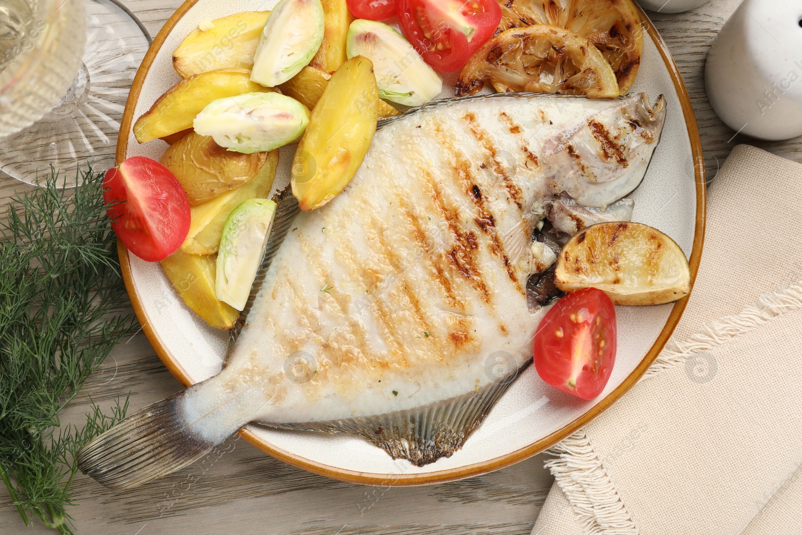 Photo of Tasty roasted flounder fish served with potatoes, tomatoes and lemon slices on light wooden table, flat lay. Homemade seafood dish