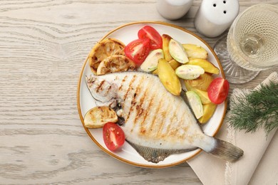 Photo of Homemade seafood dish. Tasty roasted flounder fish served with potatoes, tomatoes and lemon slices on light wooden table, flat lay. Space for text