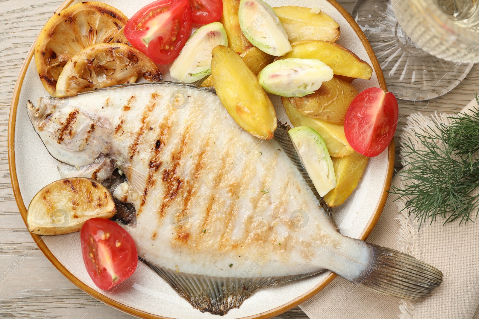 Photo of Tasty roasted flounder fish served with potatoes, tomatoes and lemon slices on light wooden table, flat lay. Homemade seafood dish