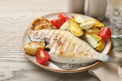 Photo of Tasty roasted flounder fish served with potatoes, tomatoes and lemon slices on light wooden table, closeup. Homemade seafood dish