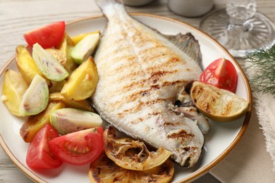 Photo of Tasty roasted flounder fish served with potatoes, tomatoes and lemon slices on light wooden table, closeup. Homemade seafood dish