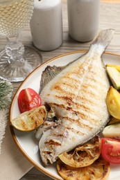 Photo of Tasty roasted flounder fish served with potatoes, tomatoes and lemon slices on light wooden table, closeup. Homemade seafood dish
