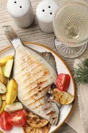Photo of Tasty roasted flounder fish served with potatoes, tomatoes and lemon slices on light wooden table, flat lay. Homemade seafood dish