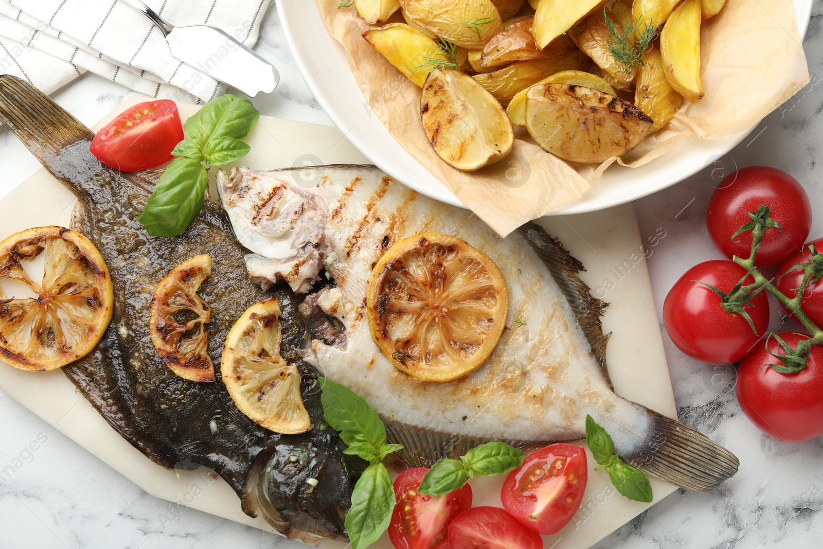 Photo of Tasty roasted flounder fish served with potatoes, tomatoes, basil and lemon slices on white marble table, flat lay. Homemade seafood dish