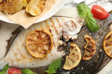 Photo of Tasty roasted flounder fish served with potatoes, tomatoes, basil and lemon slices on white marble table, flat lay. Homemade seafood dish