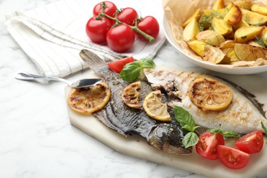 Photo of Tasty roasted flounder fish served with potatoes, tomatoes, basil and lemon slices on white marble table, closeup. Homemade seafood dish