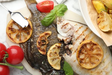 Photo of Tasty roasted flounder fish served with potatoes, tomatoes, basil and lemon slices on white marble table, flat lay. Homemade seafood dish