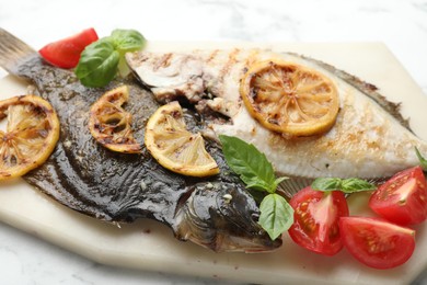 Photo of Tasty roasted flounder fish served with tomatoes, basil and lemon slices on white marble table, closeup. Homemade seafood dish