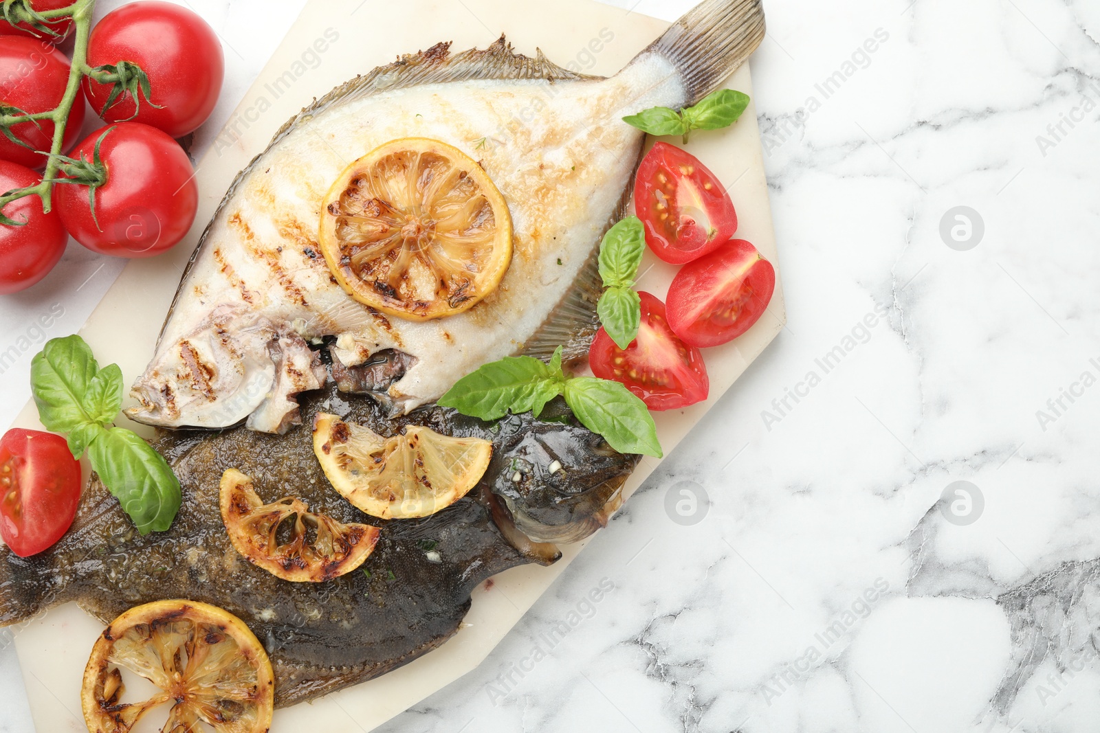Photo of Homemade seafood dish. Tasty roasted flounder fish served with tomatoes, basil and lemon slices on white marble table, flat lay. Space for text