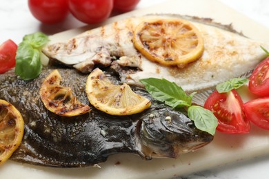 Photo of Tasty roasted flounder fish served with tomatoes, basil and lemon slices on white table, closeup. Homemade seafood dish