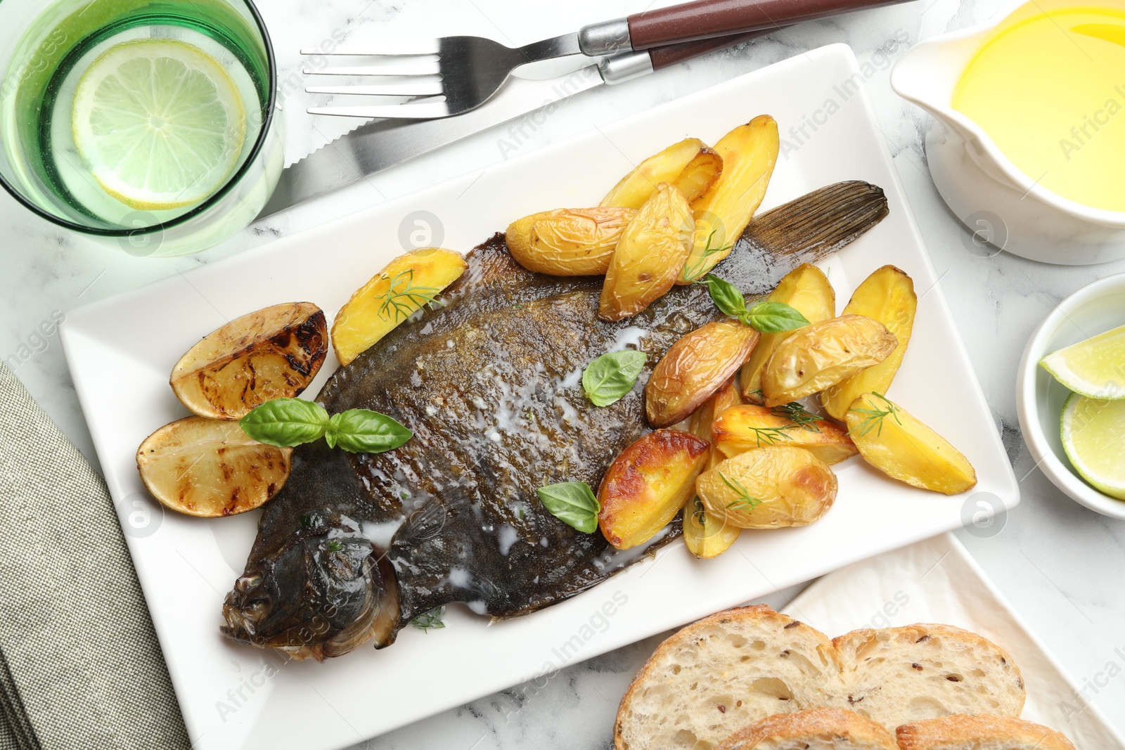 Photo of Tasty roasted flounder fish served with potatoes, basil and lemon slices on white marble table, flat lay. Homemade seafood dish