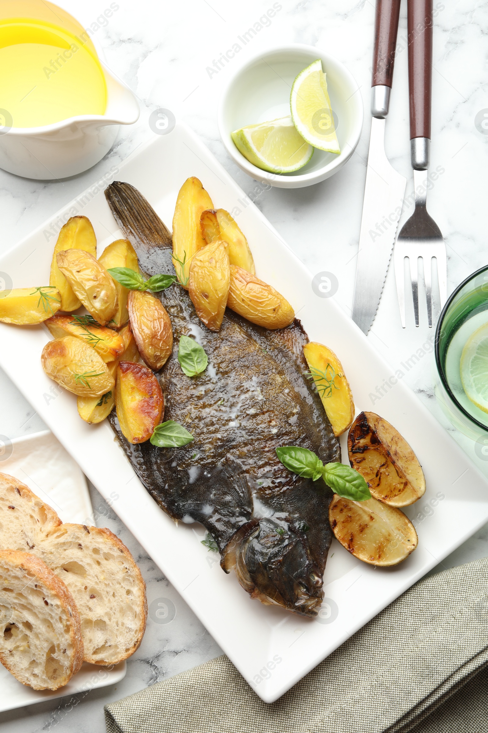 Photo of Tasty roasted flounder fish served with potatoes, basil and lemon slices on white marble table, flat lay. Homemade seafood dish