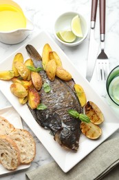 Photo of Tasty roasted flounder fish served with potatoes, basil and lemon slices on white marble table, flat lay. Homemade seafood dish