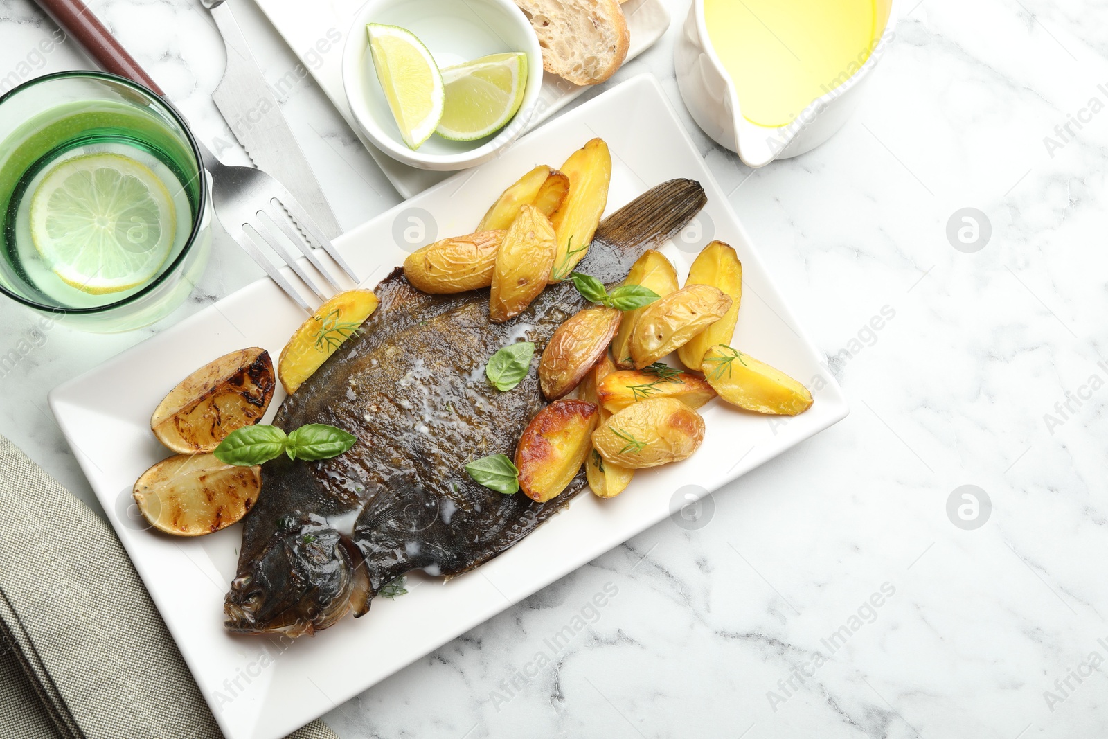 Photo of Homemade seafood dish. Tasty roasted flounder fish served with potatoes, basil and lemon slices on white marble table, flat lay. Space for text