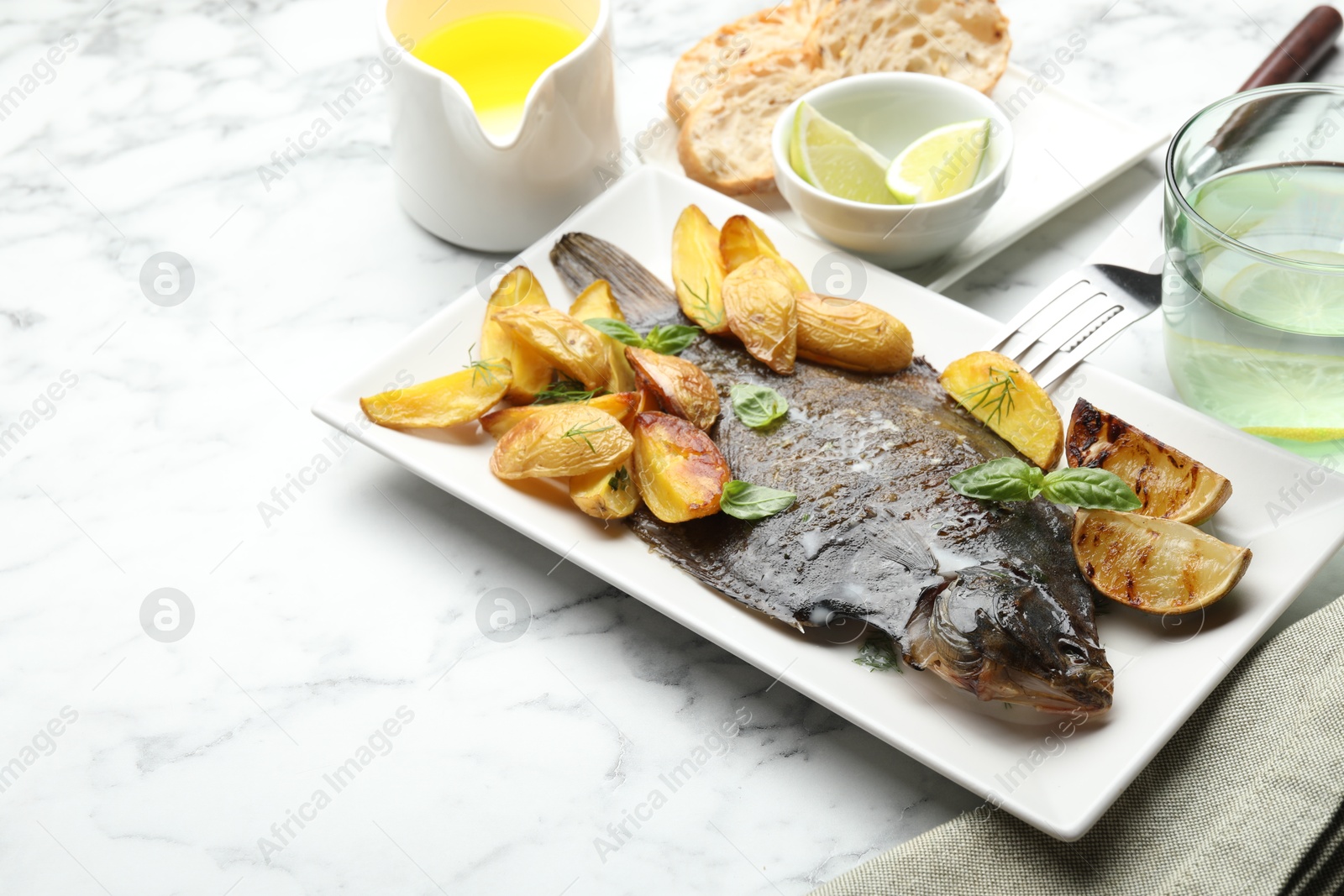 Photo of Homemade seafood dish. Tasty roasted flounder fish served with potatoes, basil and lemon slices on white marble table, closeup. Space for text