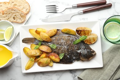 Photo of Tasty roasted flounder fish served with potatoes, basil and lemon slices on white marble table, flat lay. Homemade seafood dish
