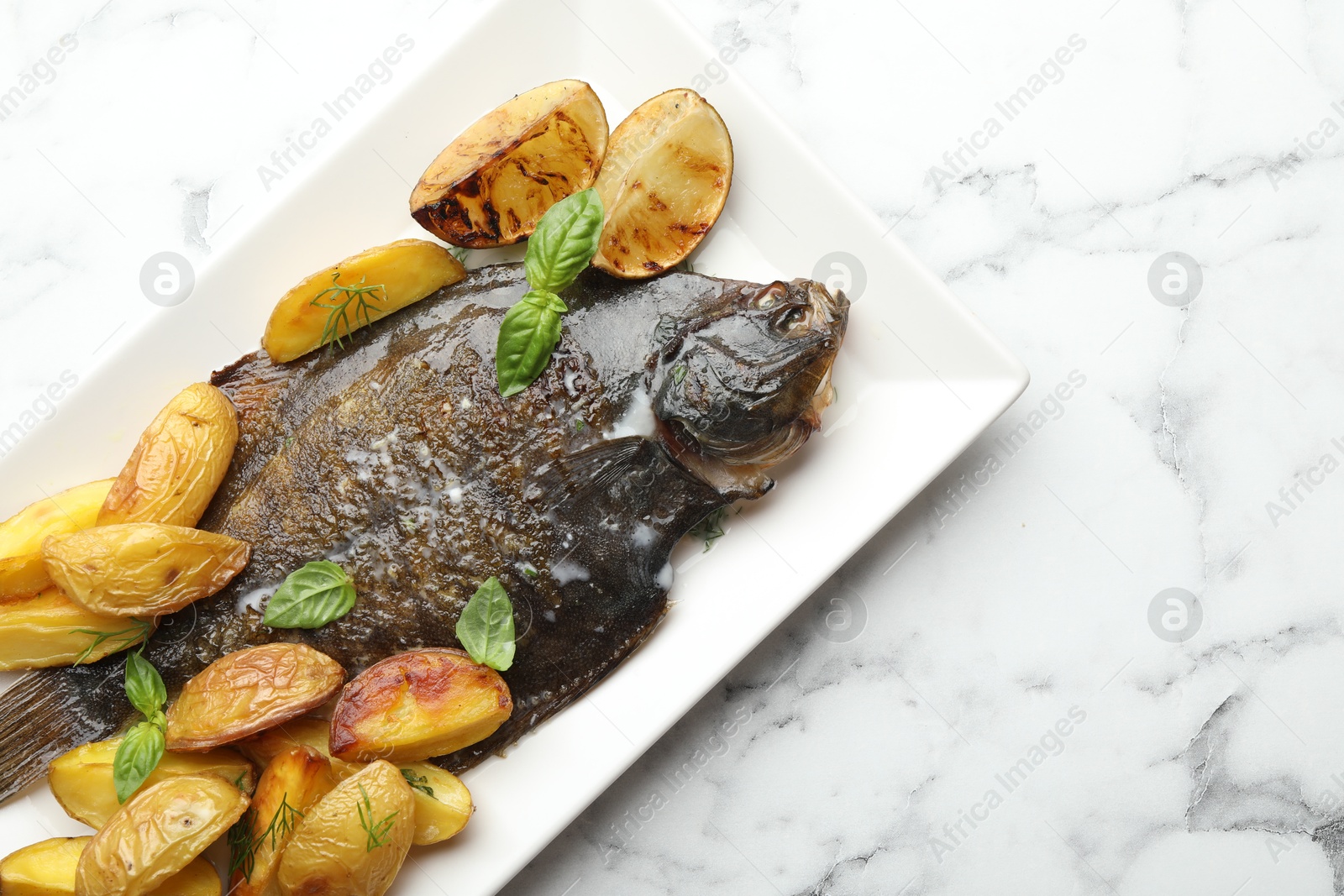 Photo of Homemade seafood dish. Tasty roasted flounder fish served with potatoes, basil and lemon slices on white marble table, top view. Space for text
