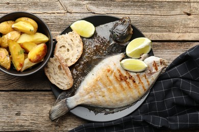 Photo of Tasty roasted flounder fish served with potatoes, bread and lime slices on wooden table, flat lay. Homemade seafood dish