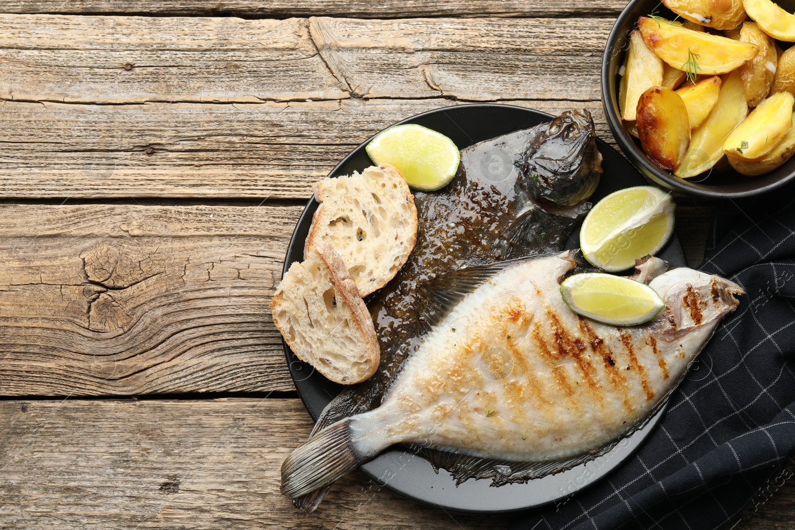 Photo of Homemade seafood dish. Tasty roasted flounder fish served with potatoes, bread and lime slices on wooden table, flat lay. Space for text