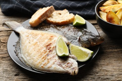 Photo of Tasty roasted flounder fish served with potatoes, bread and lime slices on wooden table, closeup. Homemade seafood dish
