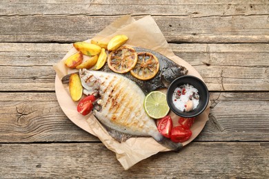 Photo of Tasty roasted flounder fish served with potatoes, tomatoes and lemon slices on wooden table, top view. Homemade seafood dish