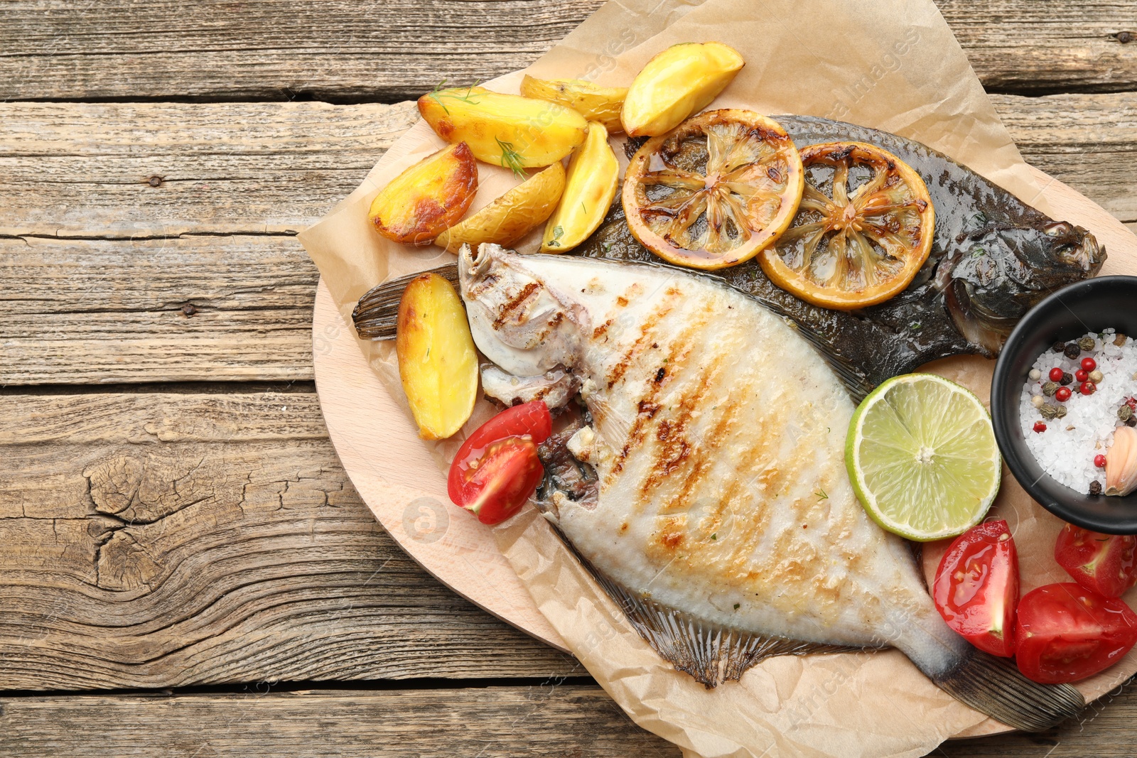 Photo of Homemade seafood dish. Tasty roasted flounder fish served with potatoes, tomatoes and lemon slices on wooden table, top view. Space for text