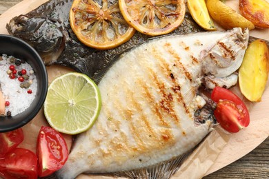 Photo of Tasty roasted flounder fish served with potatoes, tomatoes and lemon slices on wooden table, top view. Homemade seafood dish