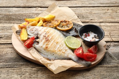 Photo of Tasty roasted flounder fish served with potatoes, tomatoes and lemon slices on wooden table, closeup. Homemade seafood dish