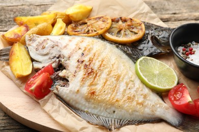 Photo of Tasty roasted flounder fish served with potatoes, tomatoes and lemon slices on wooden table, closeup. Homemade seafood dish