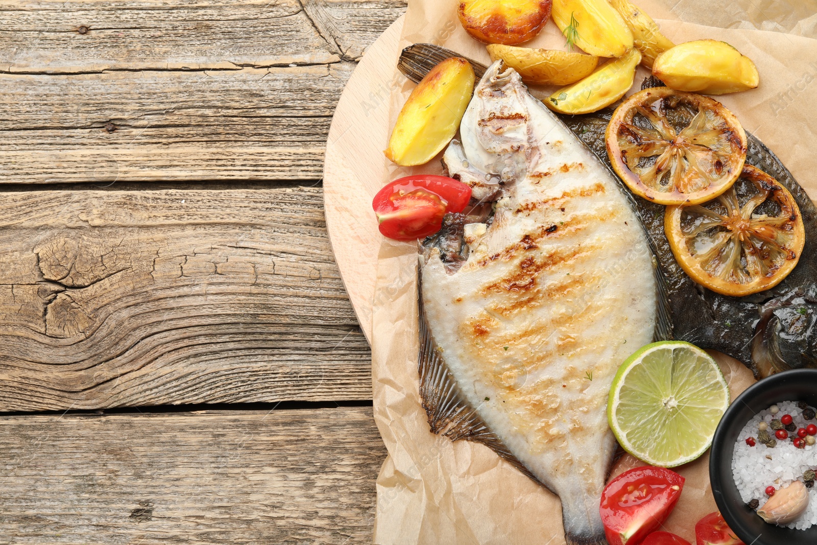 Photo of Homemade seafood dish. Tasty roasted flounder fish served with potatoes, tomatoes and lemon slices on wooden table, top view. Space for text