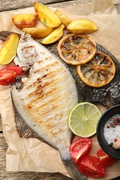 Photo of Tasty roasted flounder fish served with potatoes, tomatoes and lemon slices on wooden table, top view. Homemade seafood dish