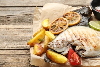 Photo of Tasty roasted flounder fish served with potatoes, tomatoes and lemon slices on wooden table, closeup. Homemade seafood dish