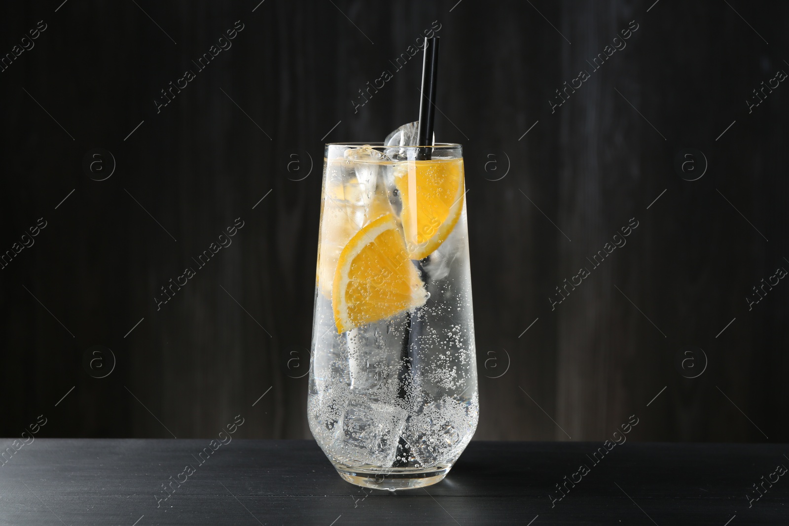 Photo of Refreshing soda water with orange slices and ice cubes in glass on black wooden table