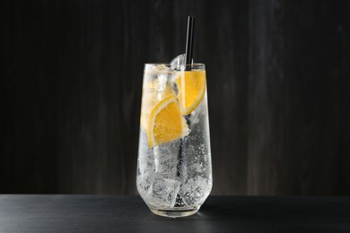Photo of Refreshing soda water with orange slices and ice cubes in glass on black wooden table