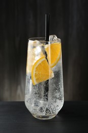 Photo of Refreshing soda water with orange slices and ice cubes in glass on black wooden table