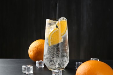 Photo of Refreshing soda water with orange slices and ice cubes on black wooden table, closeup