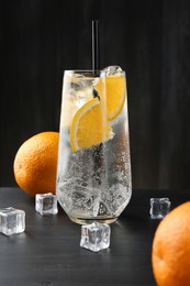 Photo of Refreshing soda water with orange slices and ice cubes on black wooden table