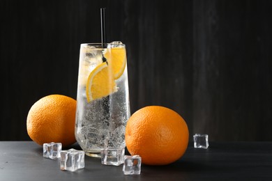 Photo of Refreshing soda water with orange slices and ice cubes on black wooden table. Space for text