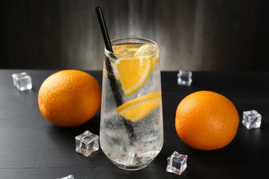 Photo of Refreshing soda water with orange slices and ice cubes on black wooden table, closeup
