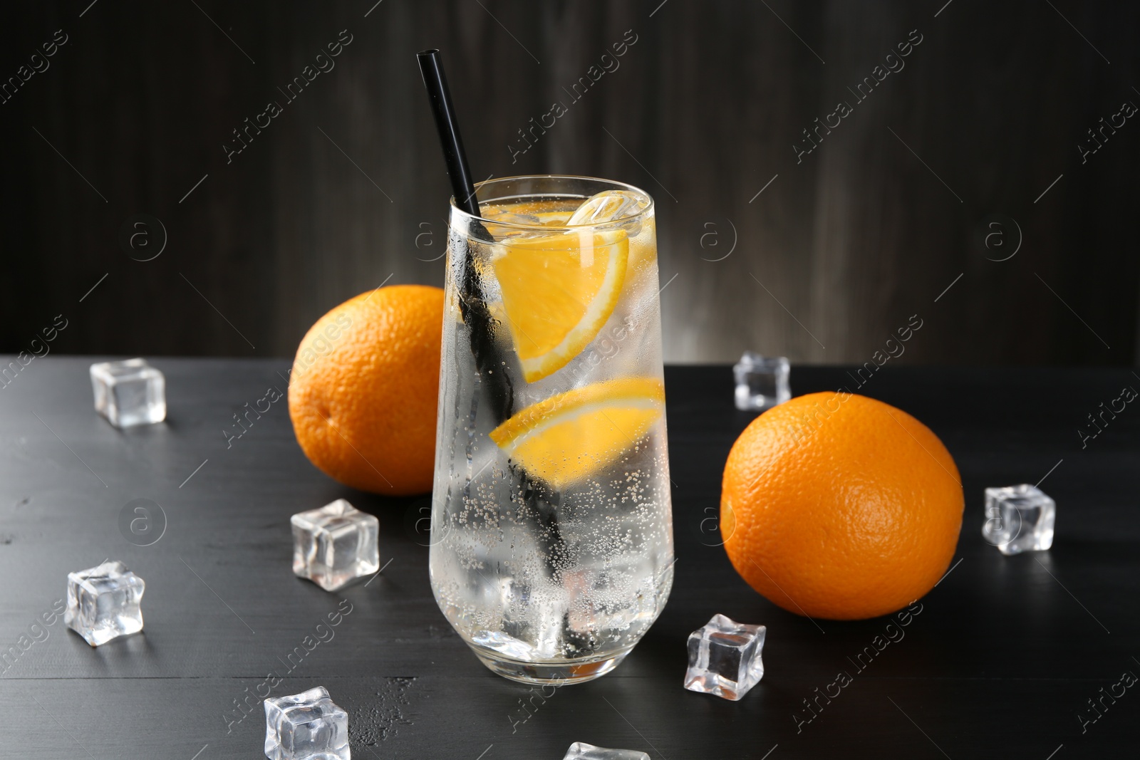 Photo of Refreshing soda water with orange slices and ice cubes on black wooden table